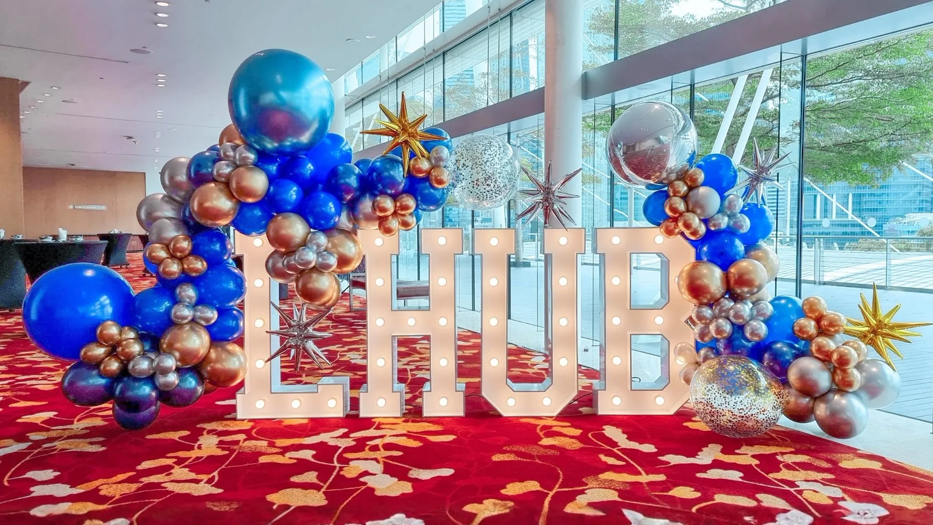 Hotel event venue entrance with large illuminated letters and blue and gold balloon styling